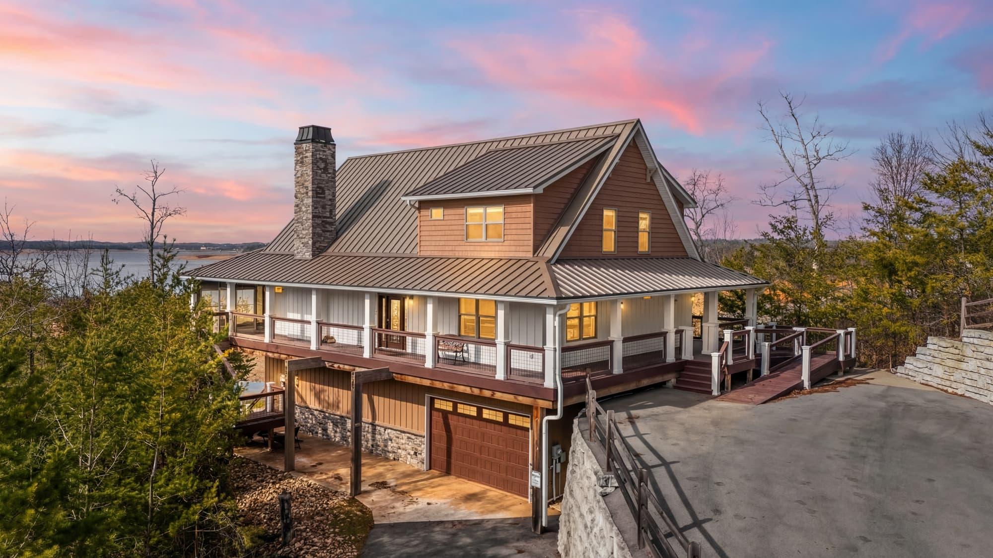 True twilight photograph of a farmhouse wraparound porch glowing under a pink dusk sky
