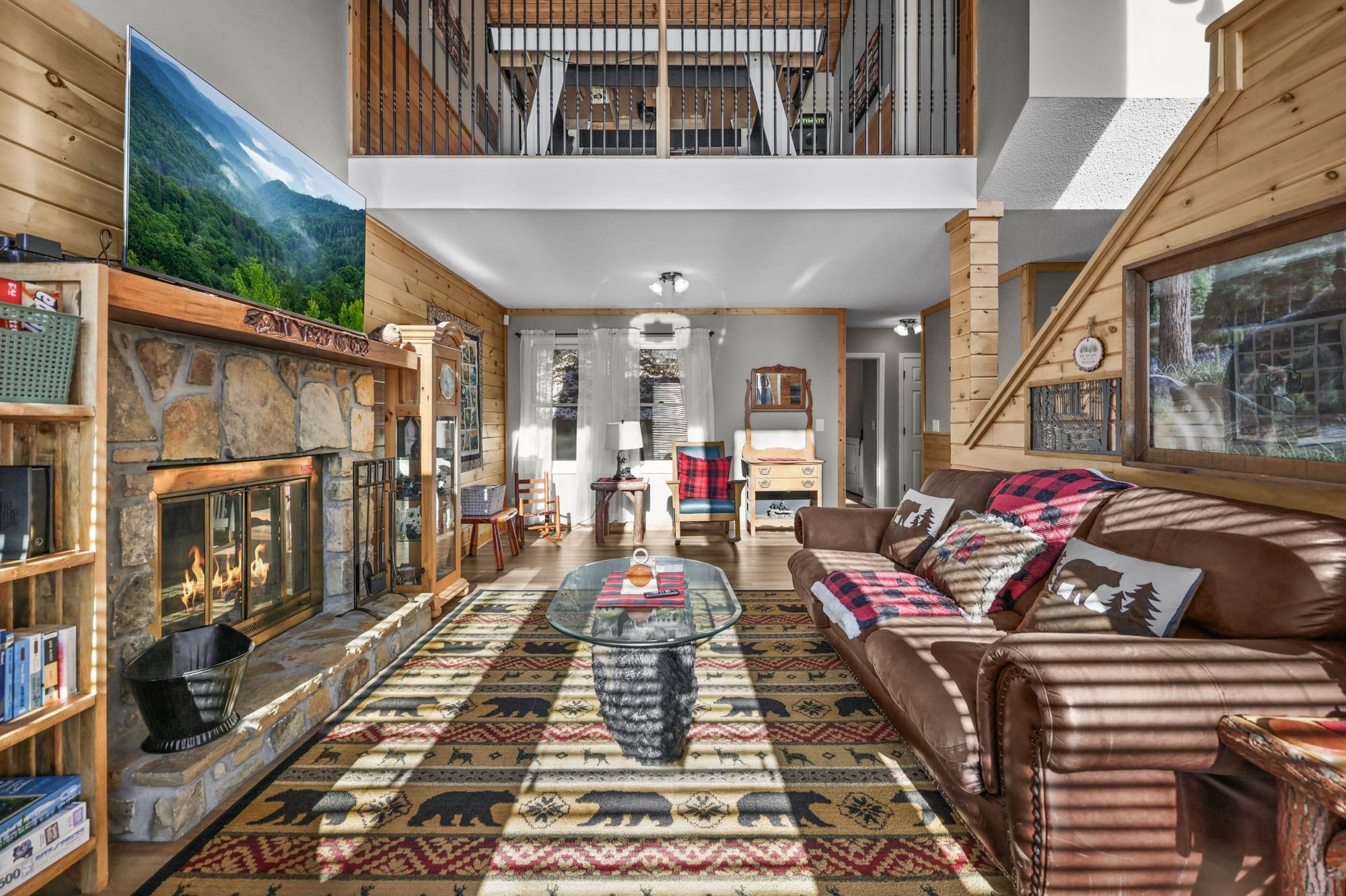 Cabin great room with lit stone fireplace and loft above