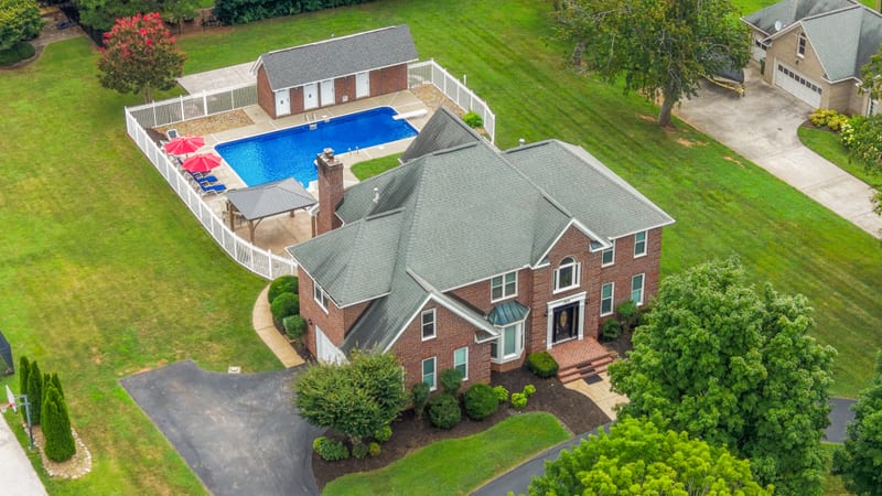 Drone aerial of a brick estate with fenced pool, pool house, and broad lawns