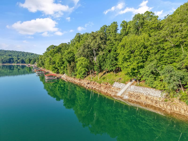 Drone view along a calm tree-lined lake shoreline with private boat docks