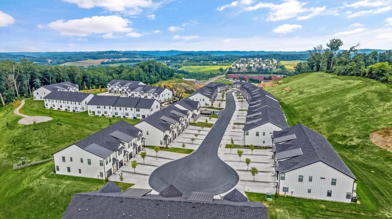 Drone aerial of a farmhouse-style townhome community winding through green hills