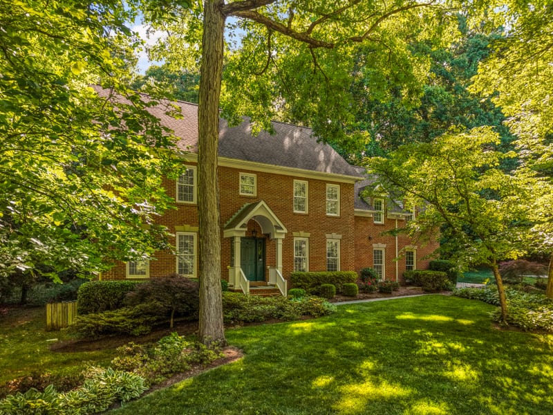 Two-story brick colonial framed by mature trees and layered landscaping