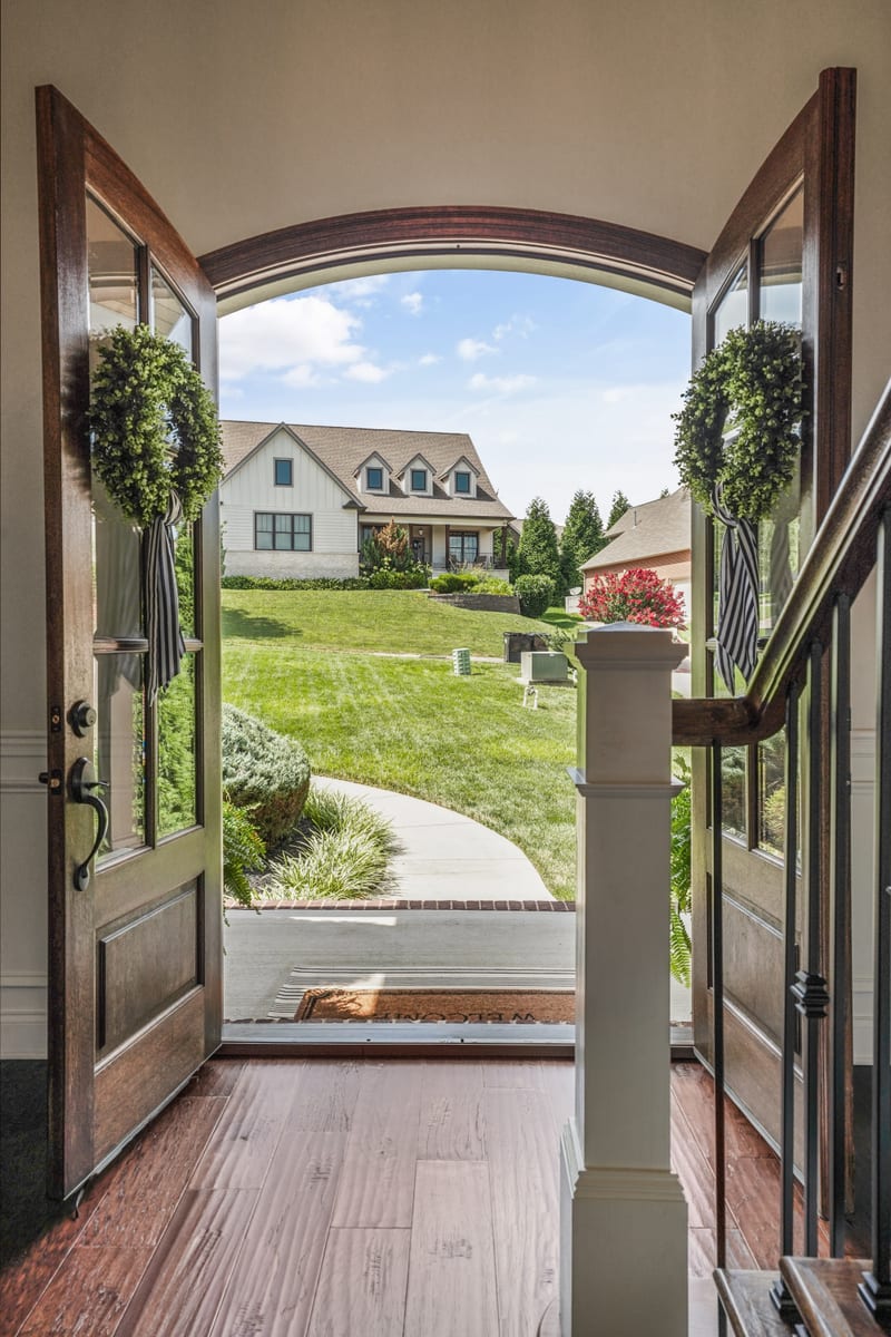 Open double front doors with wreaths framing a farmhouse across a green lawn