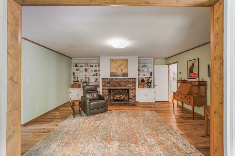 Den with brick fireplace, cedar-beam opening, and secretary desk