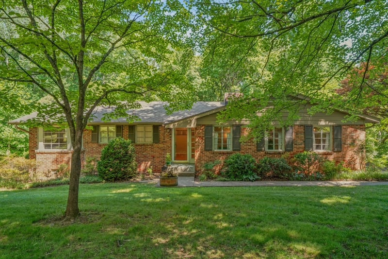 Brick ranch front under maples with warm lamp glow through the storm door