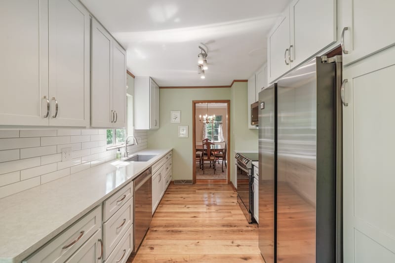 Renovated white galley kitchen with subway tile, quartz, and stainless appliances