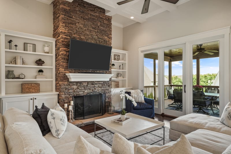 Great room with floor-to-ceiling stacked-stone fireplace, built-ins, and porch beyond