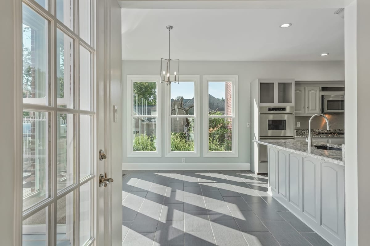 Sunlit kitchen with marble-topped island and light patterns across slate tile floors