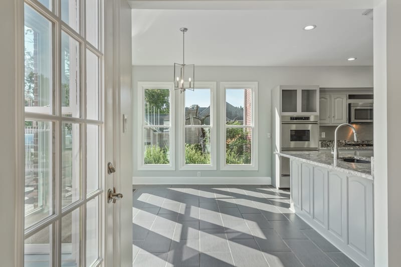 Sunlit kitchen with marble-topped island and light patterns across slate tile floors
