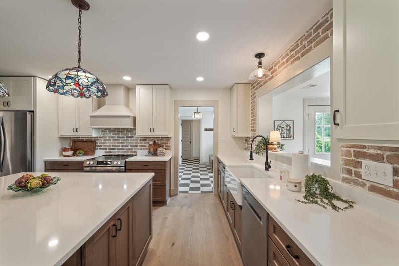 Renovated kitchen with exposed brick walls, white quartz counters, and stained-glass pendant