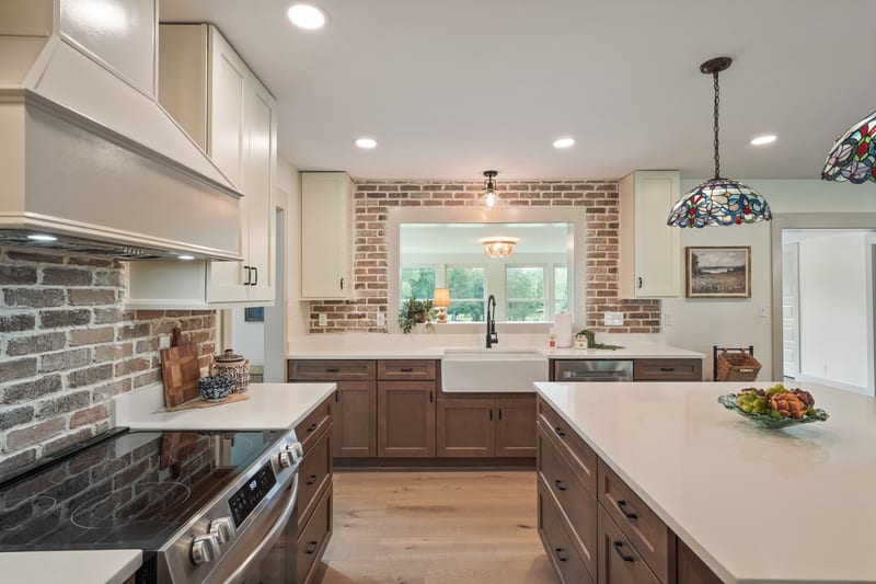 Kitchen view toward a farmhouse sink framed by exposed brick and a sunlit window