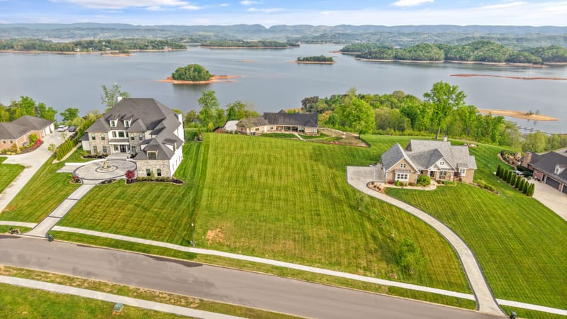 Drone aerial of a vacant green estate lot between custom homes with the lake behind
