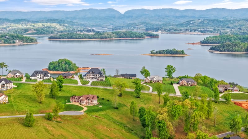 High drone aerial of a lakefront estate community with islands and mountains beyond