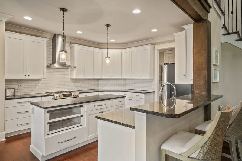 Kitchen with paired islands, vent hood, granite, and a timber beam