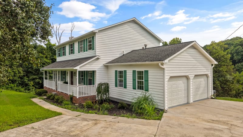 Two-story white farmhouse with green shutters and wraparound porch
