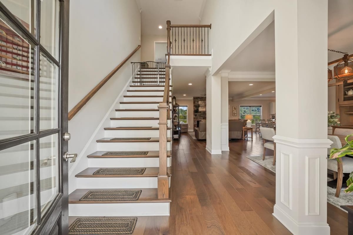Farmhouse foyer with column-framed sightline up a turned staircase