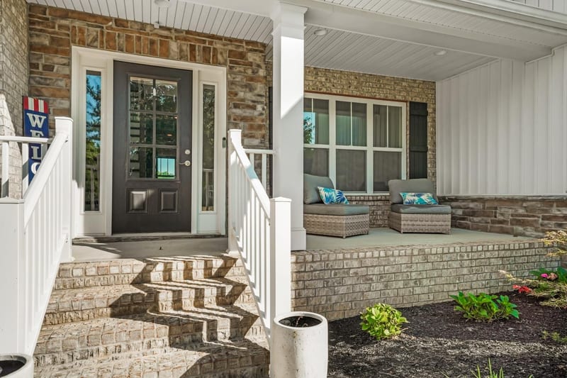 Brick front steps rising to a modern farmhouse porch with a dark door and crisp zigzag shadow