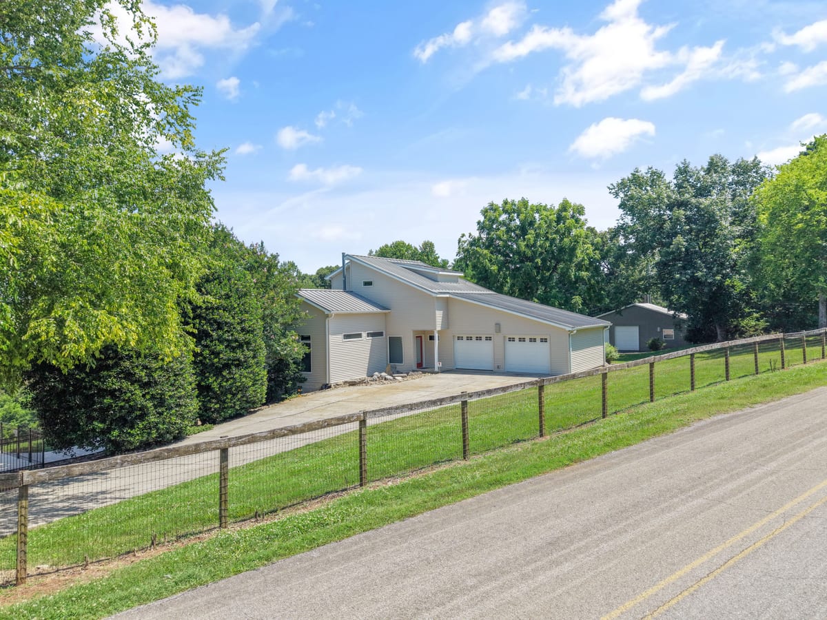 Street approach past a fenced pasture toward the hillside home