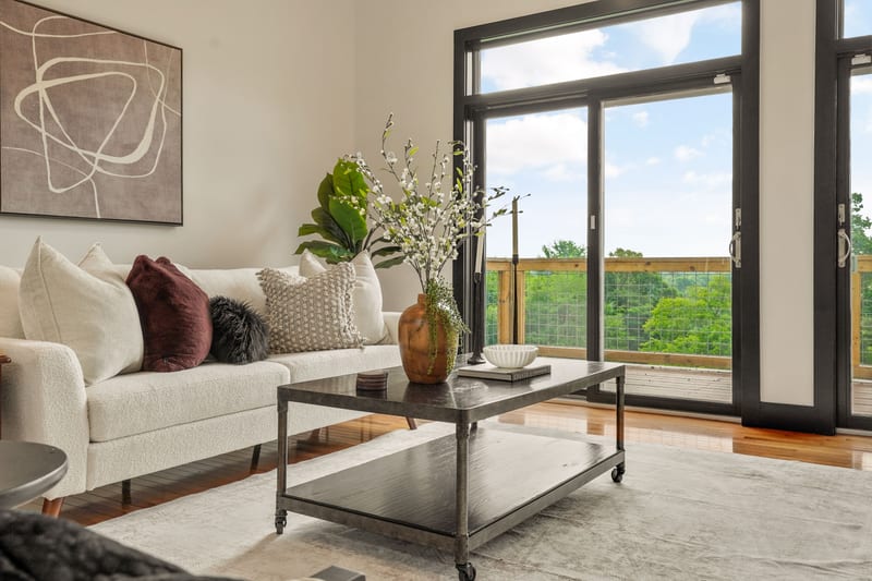 Staged living room with black sliding doors open to a treetop view