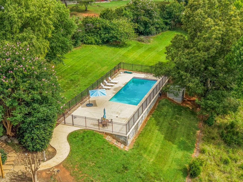 Drone aerial of the fenced pool, crape myrtle, and curved walkway