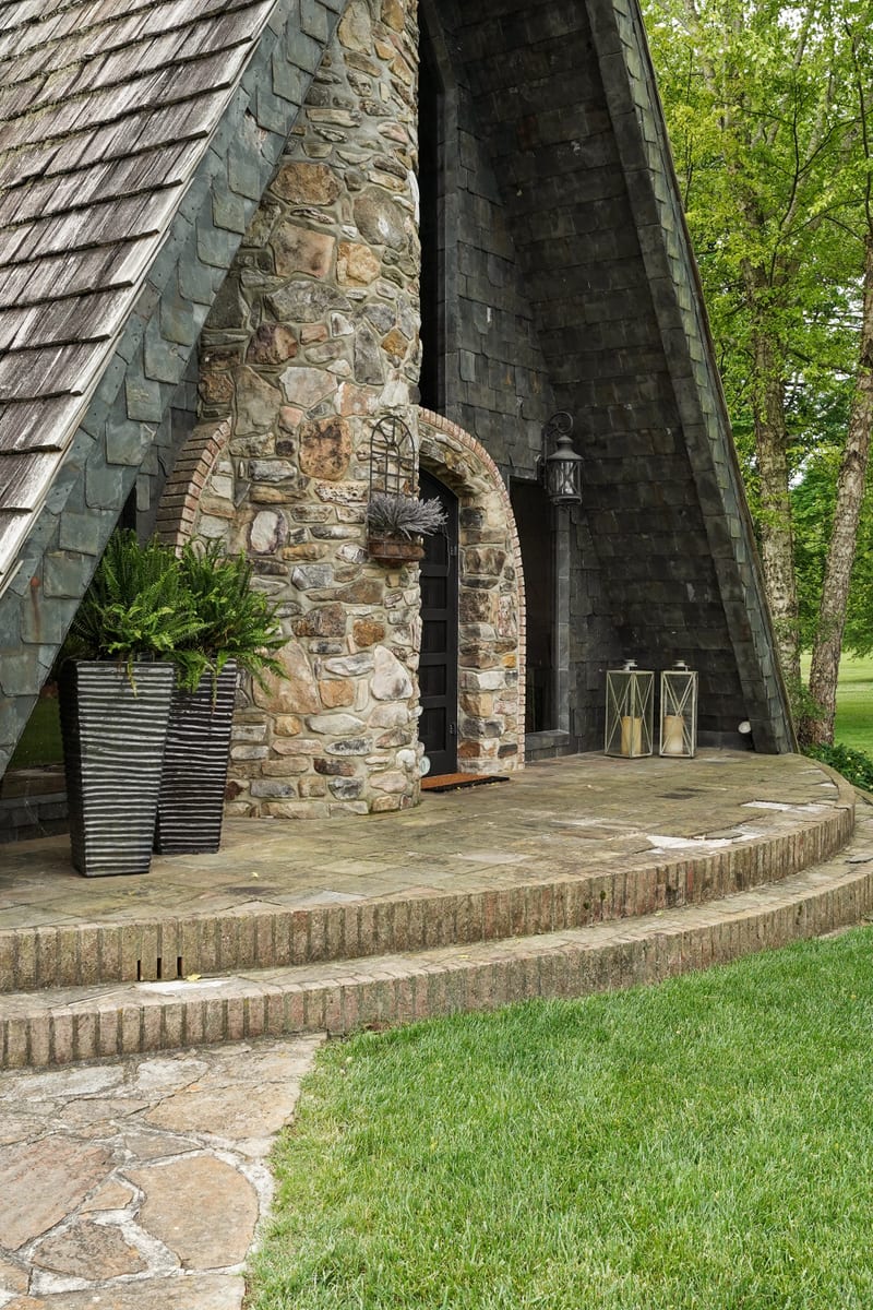 Dramatic stone A-frame entry with arched doorway, lanterns, and slate roof