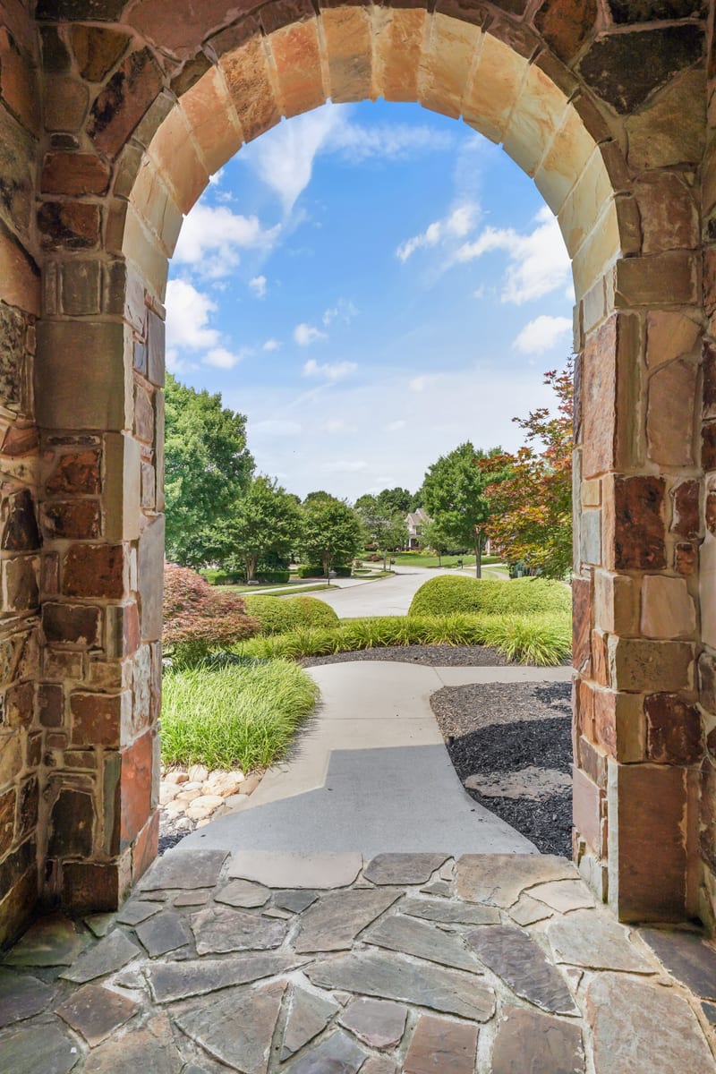 View through a stacked-stone entry archway toward a landscaped front walk