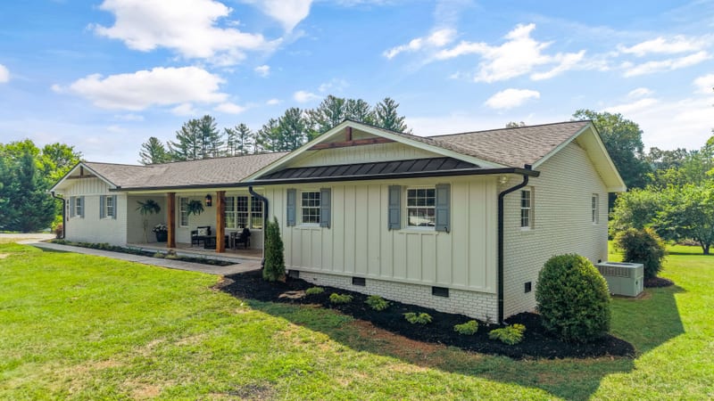 Front three-quarter view of a white-brick board-and-batten ranch with cedar porch posts