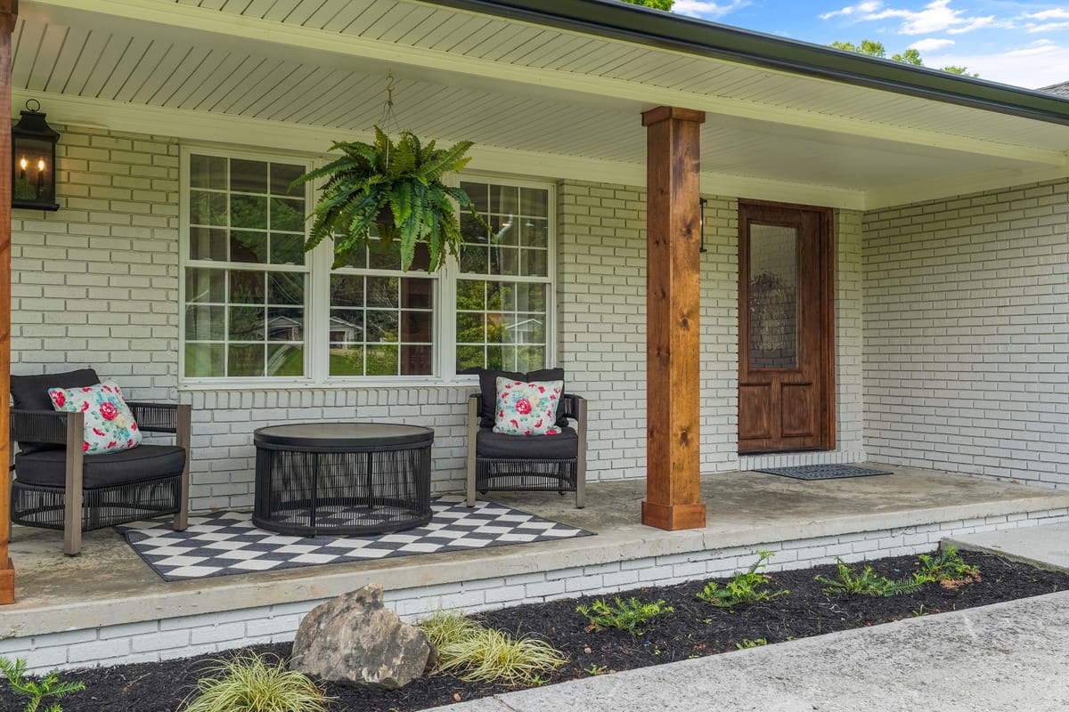 Black rockers on a checkerboard rug with a fern on a white farmhouse porch
